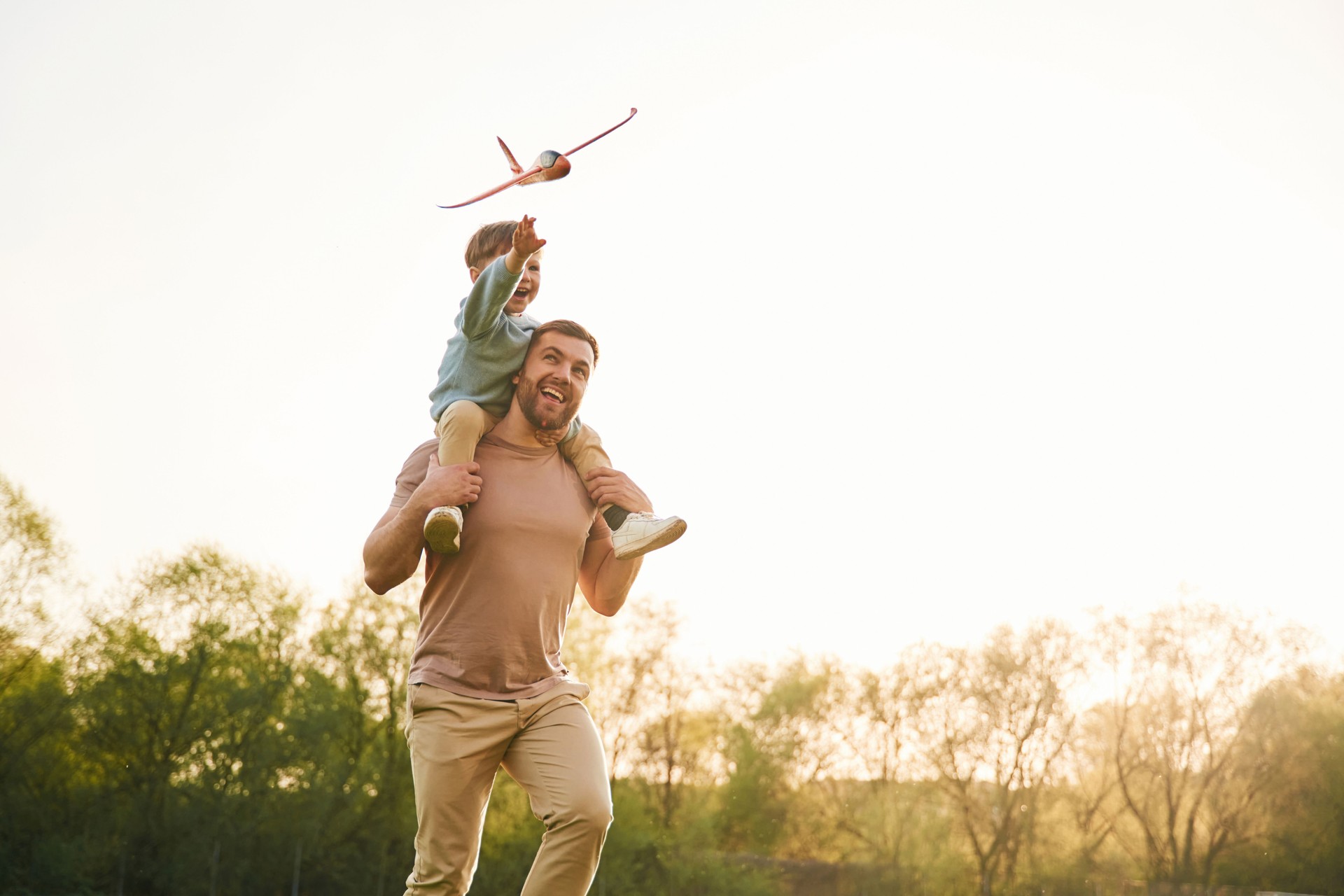 Toy plane is in the air. Happy father with son are having fun on the field at summertime